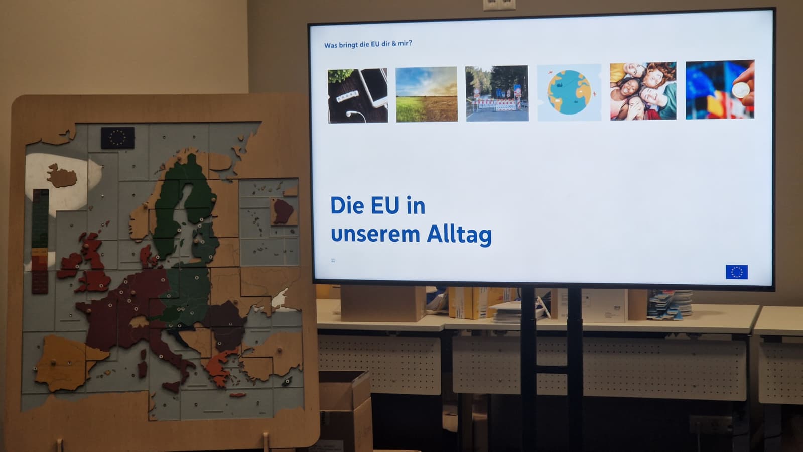 Hölzernes Europa-Puzzle neben einem Bildschirm mit dem Titel „Die EU in unserem Alltag“
