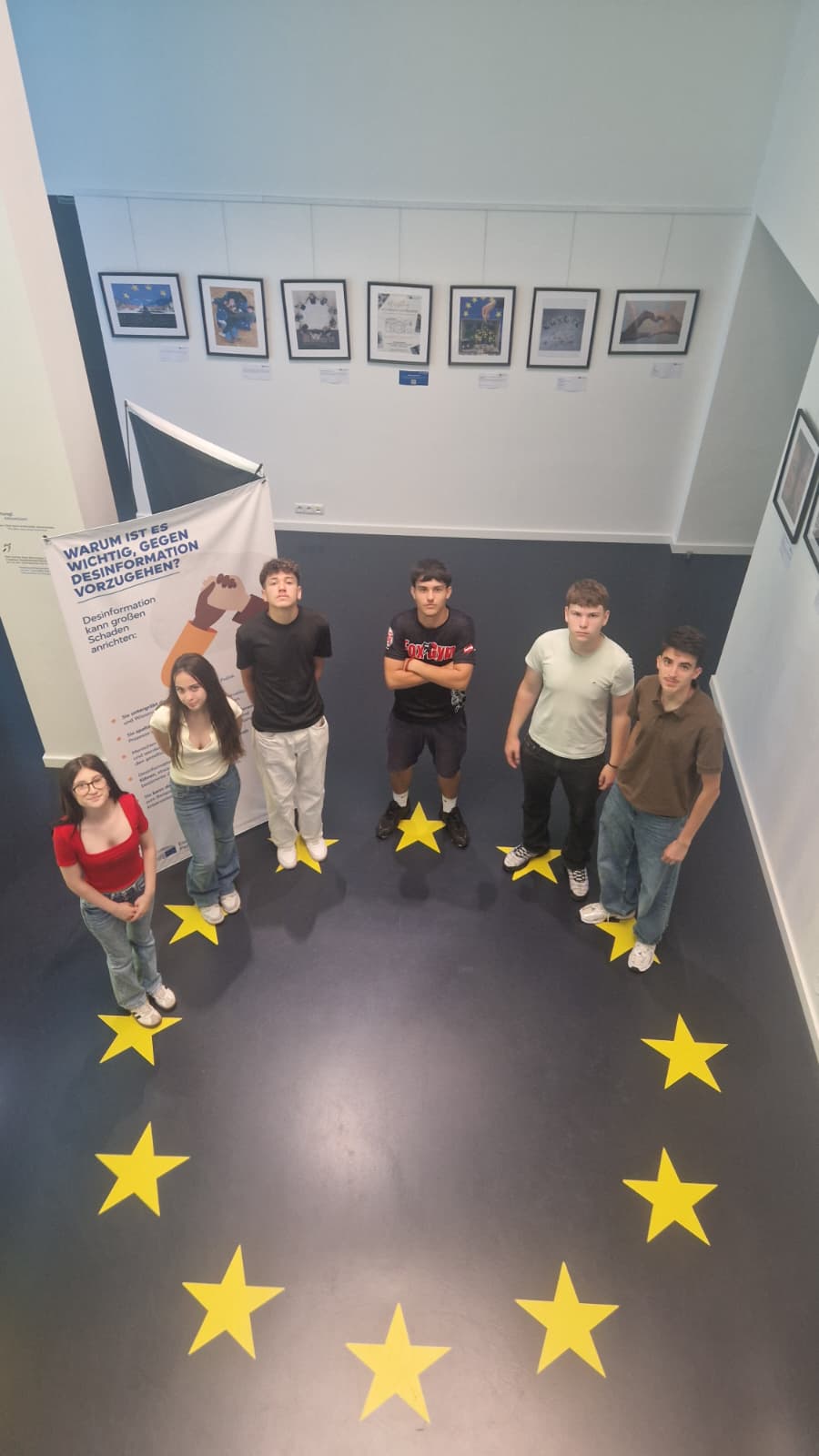 Schülerinnen und Schüler stehen im Kreis der zwölf EU-Sterne vor einem Plakat über Desinformation