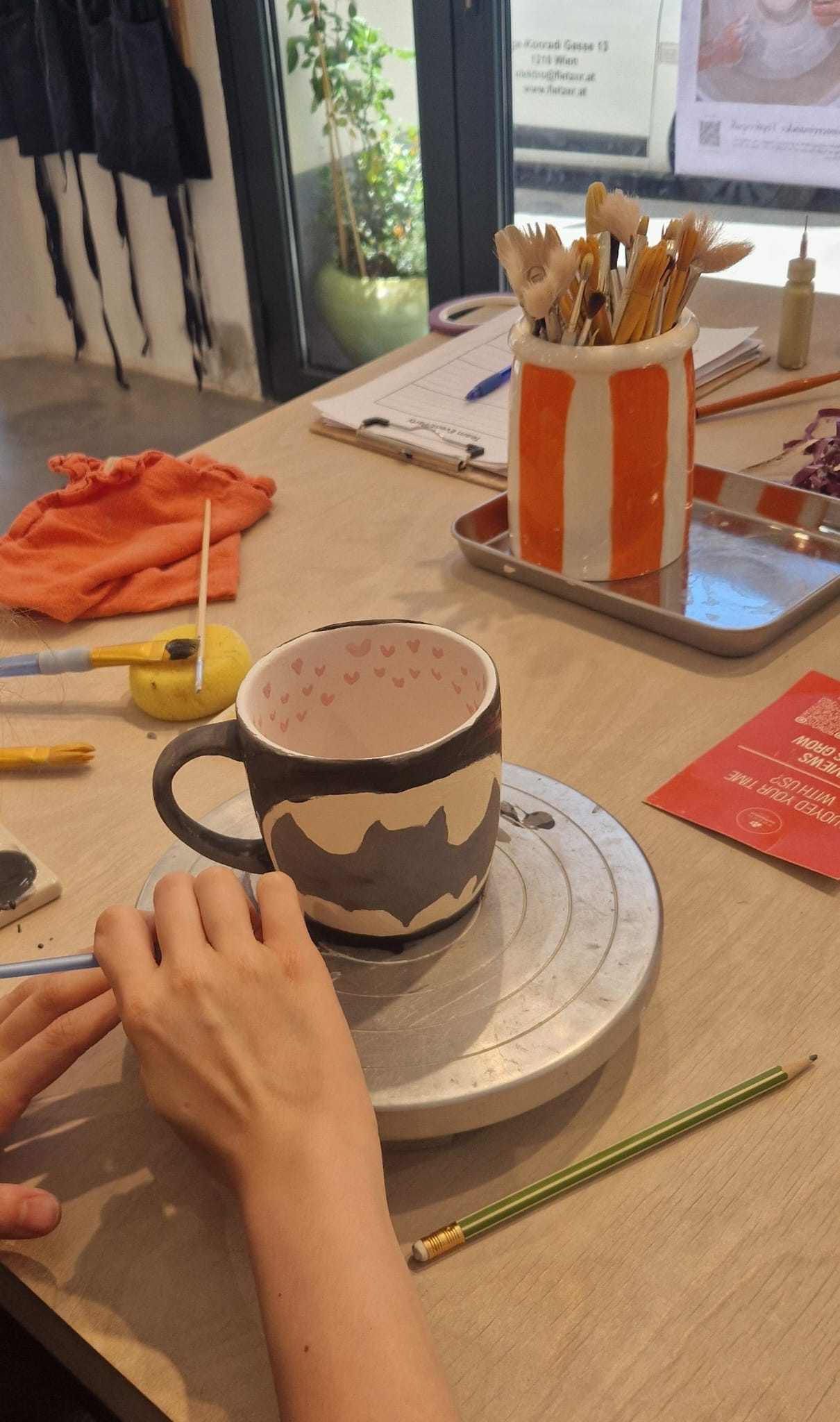 Eine Keramiktasse wird mit schwarzem Muster und kleinen Herzen im Inneren bemalt