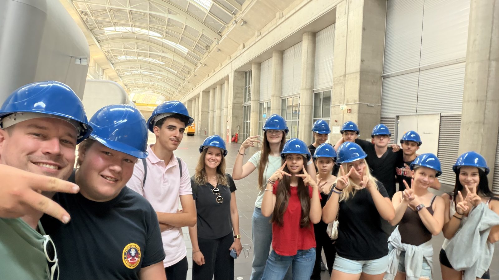 Fröhliches Gruppen-Selfie der PTS Ebreichsdorf mit blauen Schutzhelmen in der Maschinenhalle des Kraftwerks Freudenau