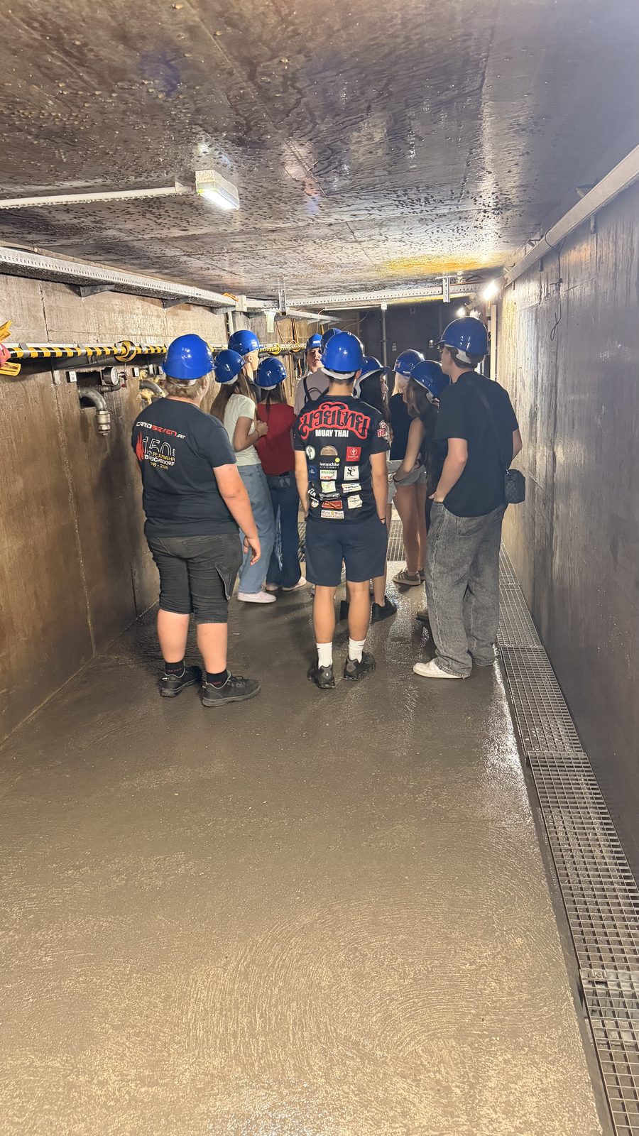 Schüler:innen mit Schutzhelmen gehen durch einen engen Betontunnel im Kraftwerk Freudenau
