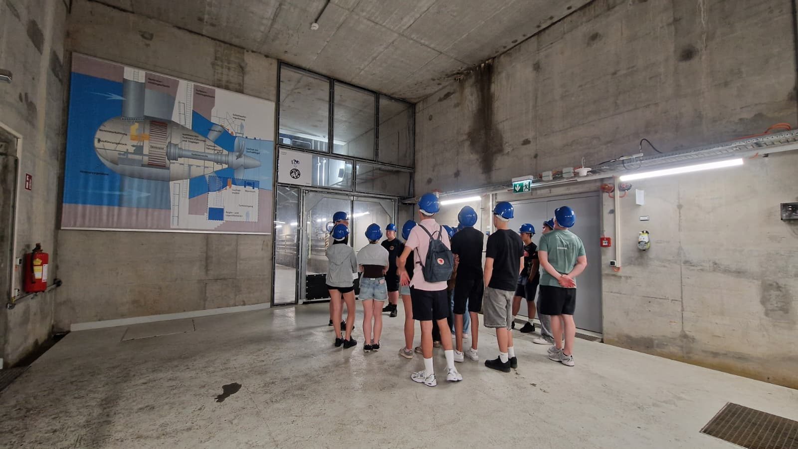 Schüler:innen der PTS Ebreichsdorf mit blauen Schutzhelmen betrachten eine Schautafel einer Kaplan-Turbine im Kraftwerk Freudenau