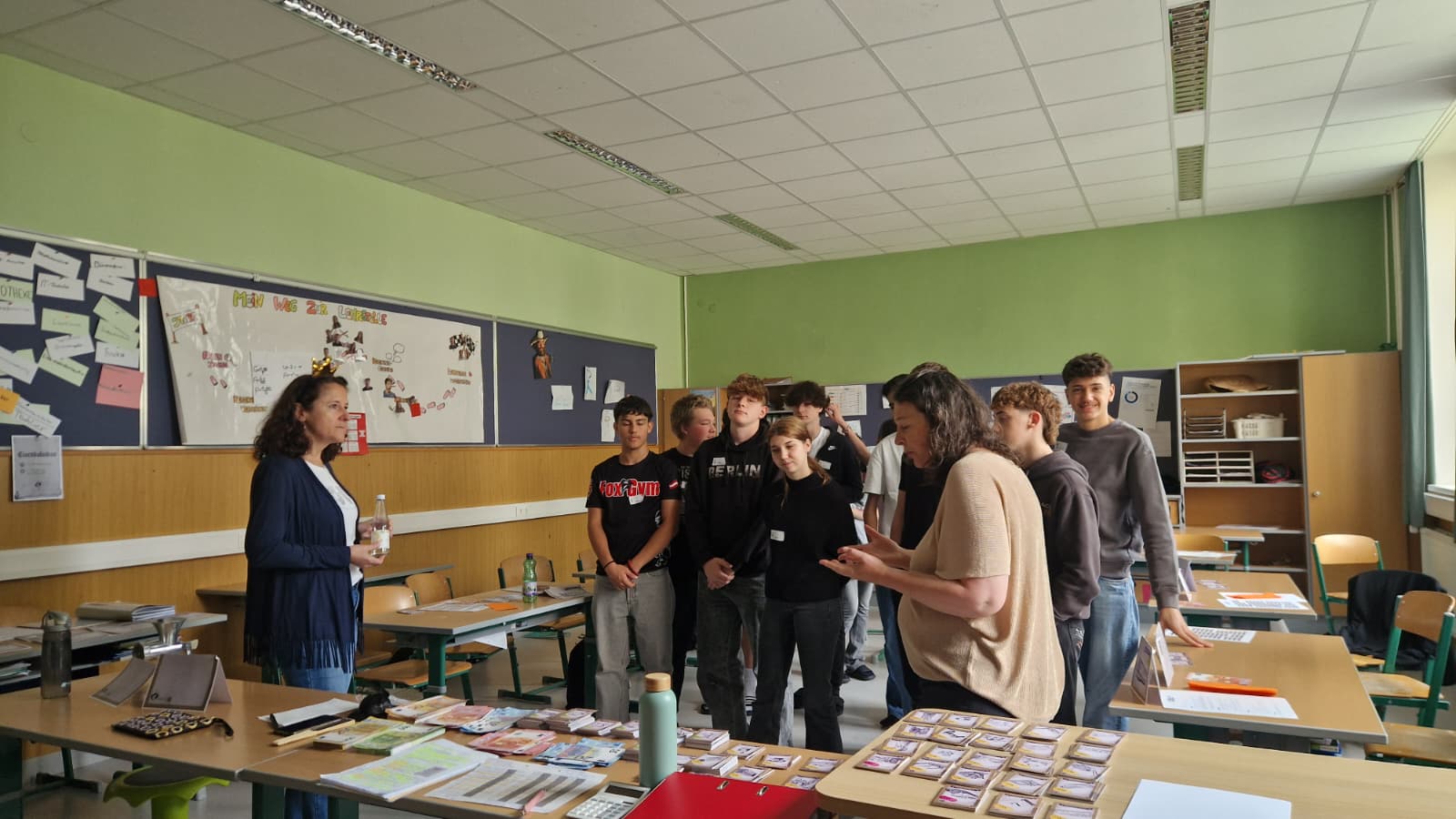 Schüler:innen besprechen mit der AK-Trainerin die Spielmaterialien des Planspiels Sozialstaat